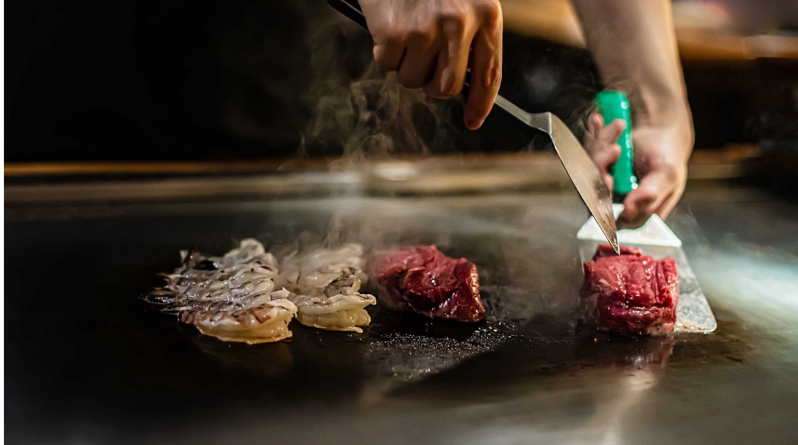 un abile cuoco gira abilmente la carne e i dim sum sulla piastra calda del teppanyaki con la spatola