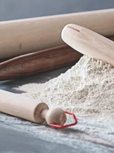 Matterello in legno e montagnetta di farina sulla spianatoria di marmo. intorno, altri tre matterelli di dimensioni diverse