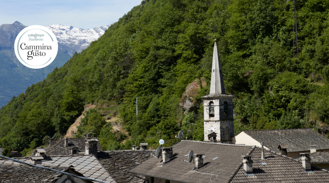 Tetti in pietra di un borgo valdostano con un campanile storico e montagne innevate sullo sfondo.