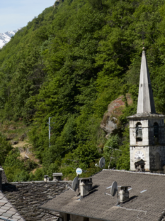 Tetti in pietra di un borgo valdostano con un campanile storico e montagne innevate sullo sfondo.