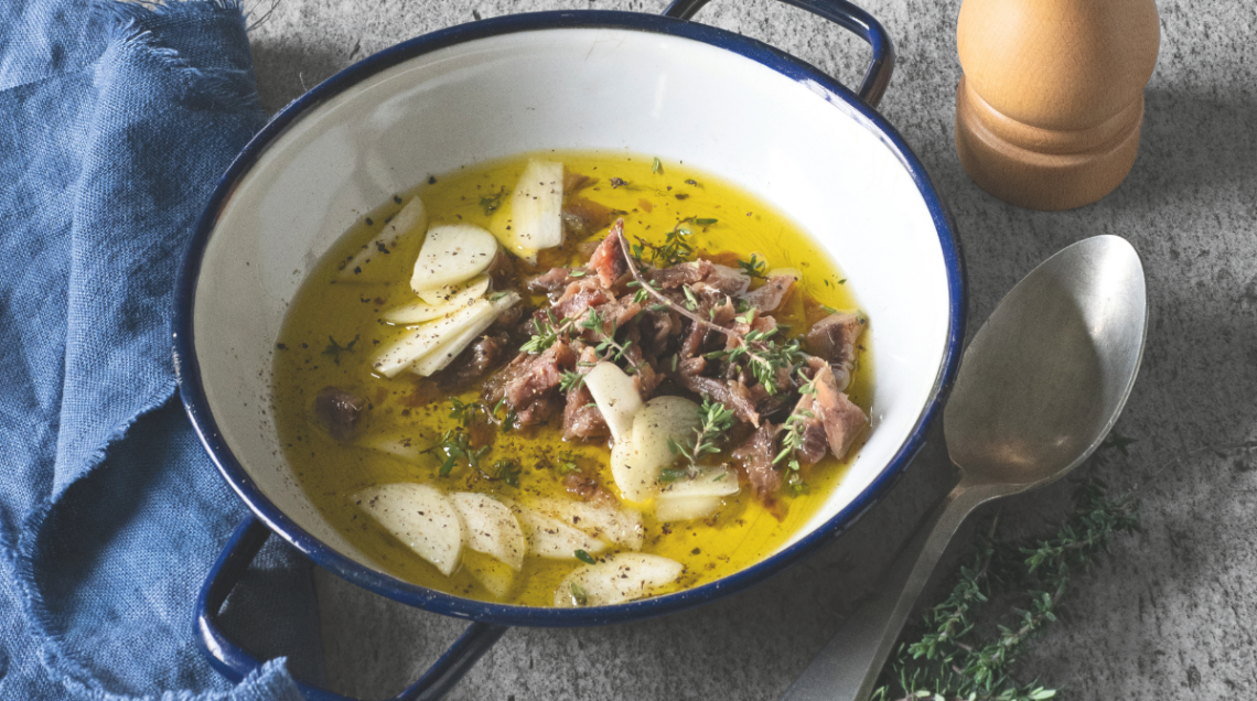 Filetti di acciughe o aringhe sott'olio con spicchi d'aglio e timo fresco in un piatto smaltato bianco e blu, simbolo dell'elogio del poco ma buono a tavola.