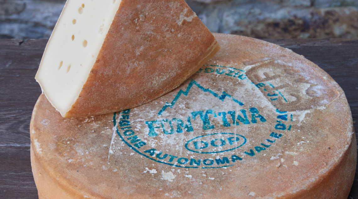 Intera forma di Fontina DOP con marchio impresso e uno spicchio tagliato appoggiato sopra.