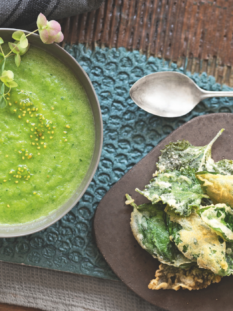 gazpacho verde dentro un piatto fondo e tempura di foglie di basilico e perilla su tagliere grigio