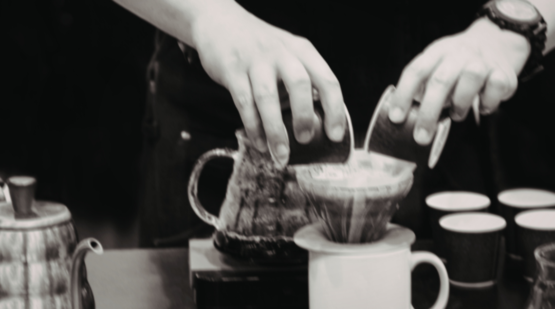 Foto in bianco e nero di un barista che prepara un caffè filtro manuale versando l'acqua con precisione.