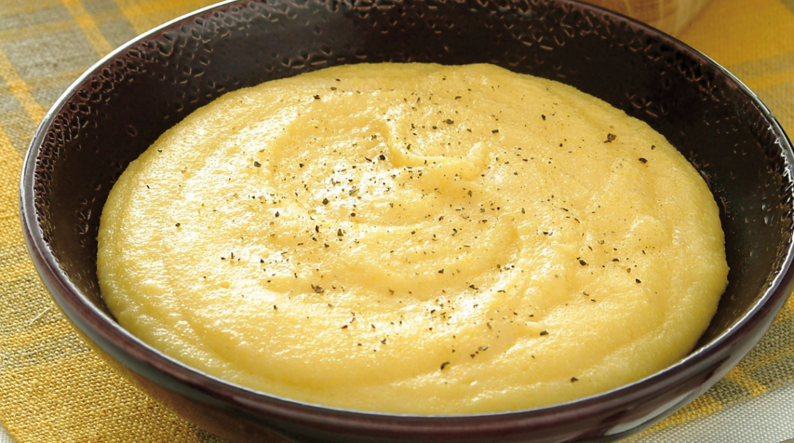 Ciotola scura con fumante polenta concia valdostana condita con pepe nero.