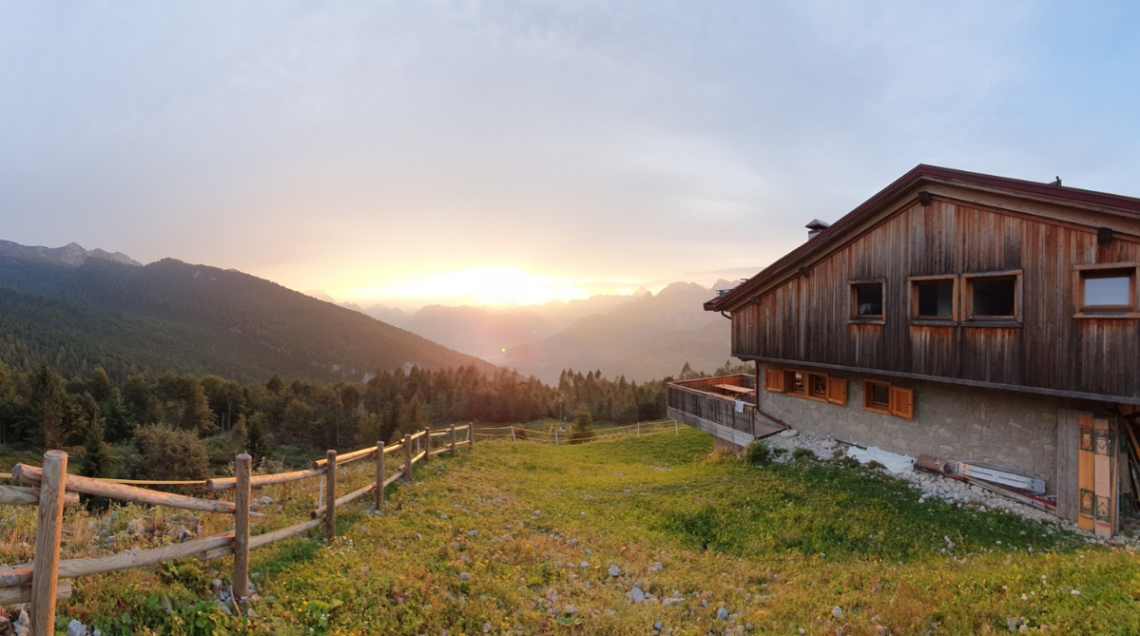 Il Rifugio Pradut di Claut in legno e pietra affacciato su una vallata alpina durante i colori caldi del tramonto.