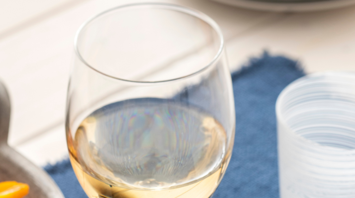 Dettaglio di un calice di vino bianco fermo dai riflessi dorati appoggiato su una tovaglietta blu.