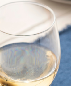 Dettaglio di un calice di vino bianco fermo dai riflessi dorati appoggiato su una tovaglietta blu.