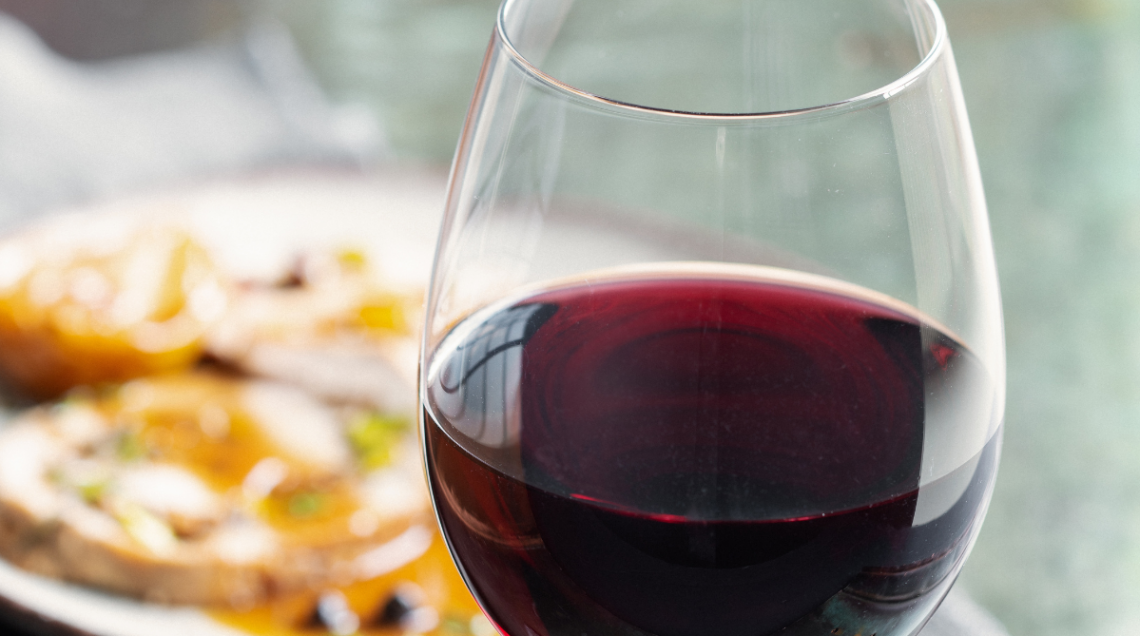 Calice in primo piano con vino rosso corposo valdostano Petit Rouge, con piatto sfocato sullo sfondo.