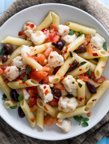 Su un piatto fondo bianco delle penne alle olive, pomodori e rana pescatrice