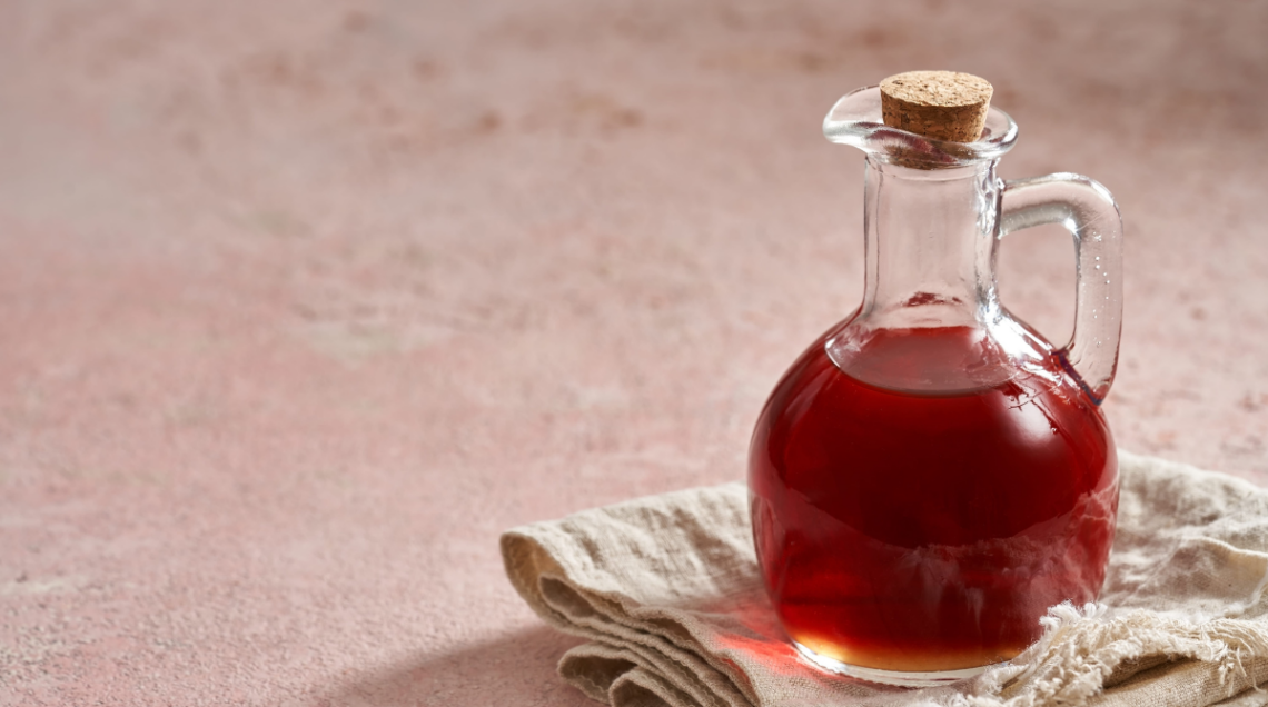 sfondo rosa con boccetta elegante colma di un condimento liquido denso rosso (agresto), appoggiata su un tovagliolo di lino,