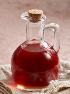 sfondo rosa con boccetta elegante colma di un condimento liquido denso rosso (agresto), appoggiata su un tovagliolo di lino,