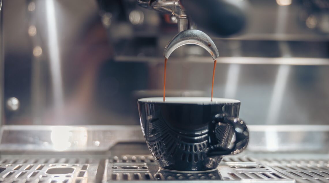 Il caffè: primo piano di una tazzina che viene riempita nella macchina del bar