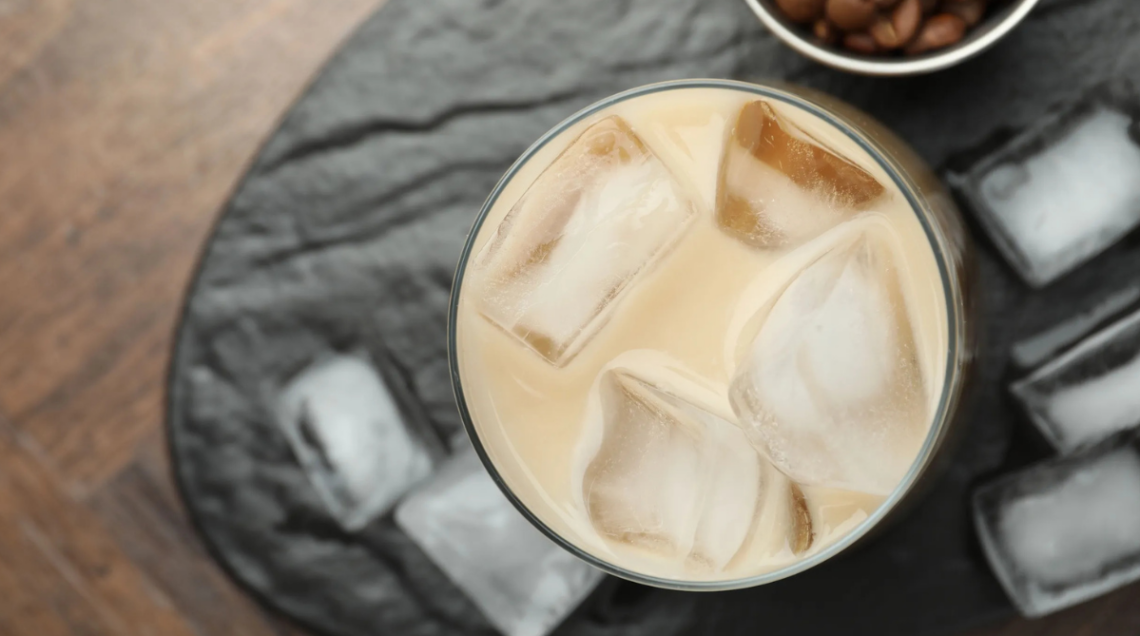 Caff&egrave; freddo all'interno di un bicchiere su tagliere con quadretti di ghiaccio