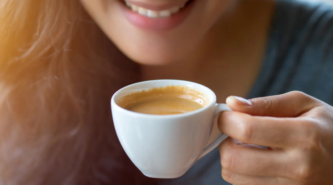 Tazzina di caff&egrave; bianca tenuta in mano da una ragazza che sorride
