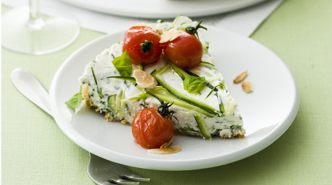 Cheesecake salato alle zucchine su piatto bianco, decorato con tre pomodorini