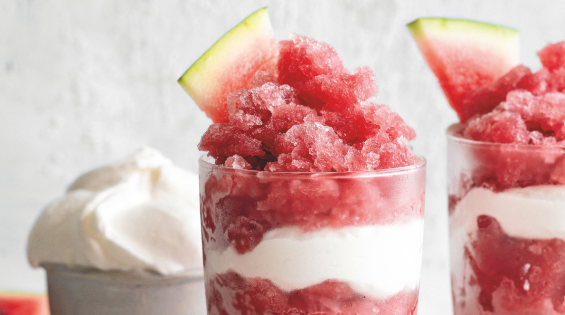 due bicchieri di vetro trasparente con granita di anguria, vino rosso e panna montata decorati con fettine di anguria