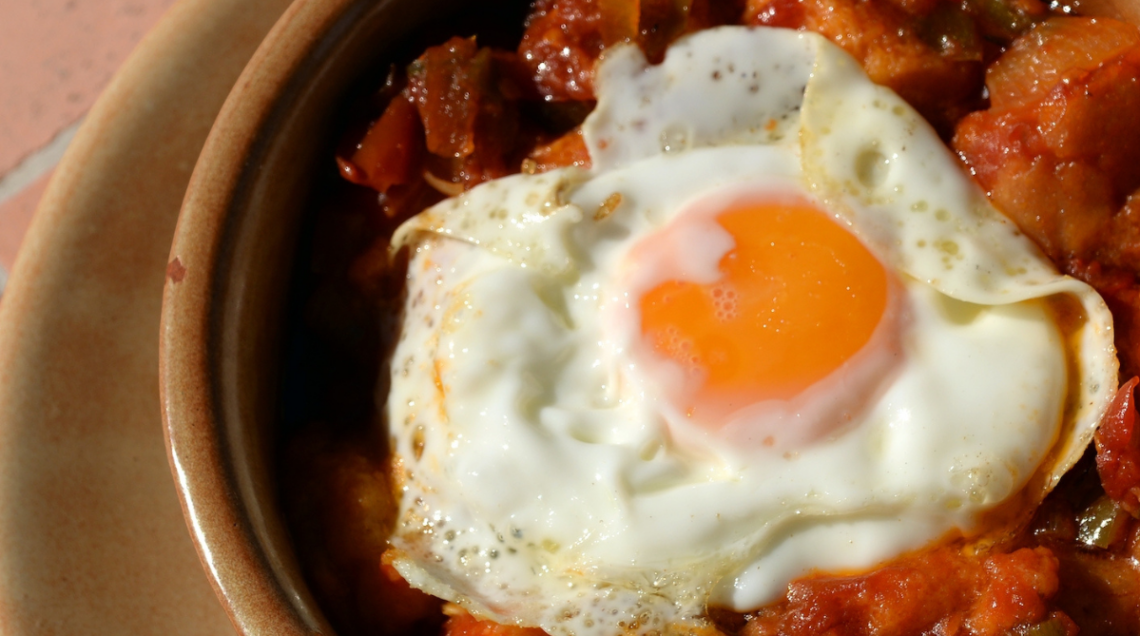Huevos a la flamenca serviti in un tegame di terracotta, con un uovo all'occhio di bue adagiato su una base di sugo al pomodoro e chorizo.