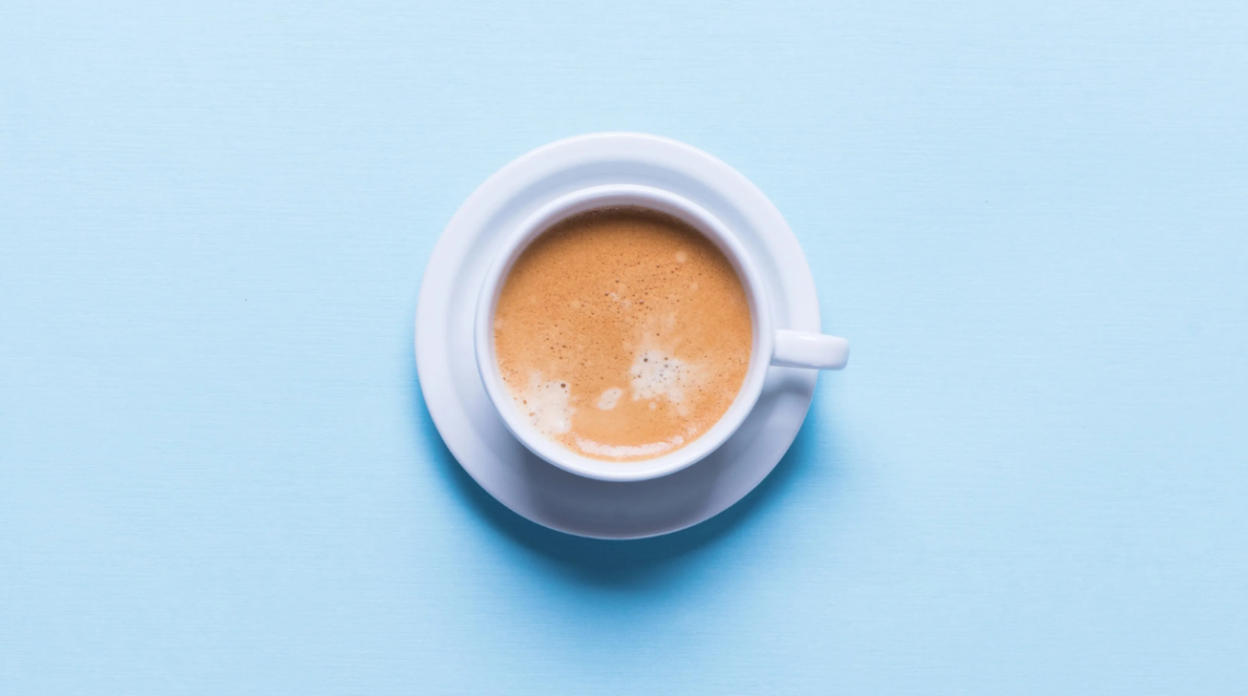Caff&egrave; macchiato all'interno di una tazzina bianca su sfondo azzurro
