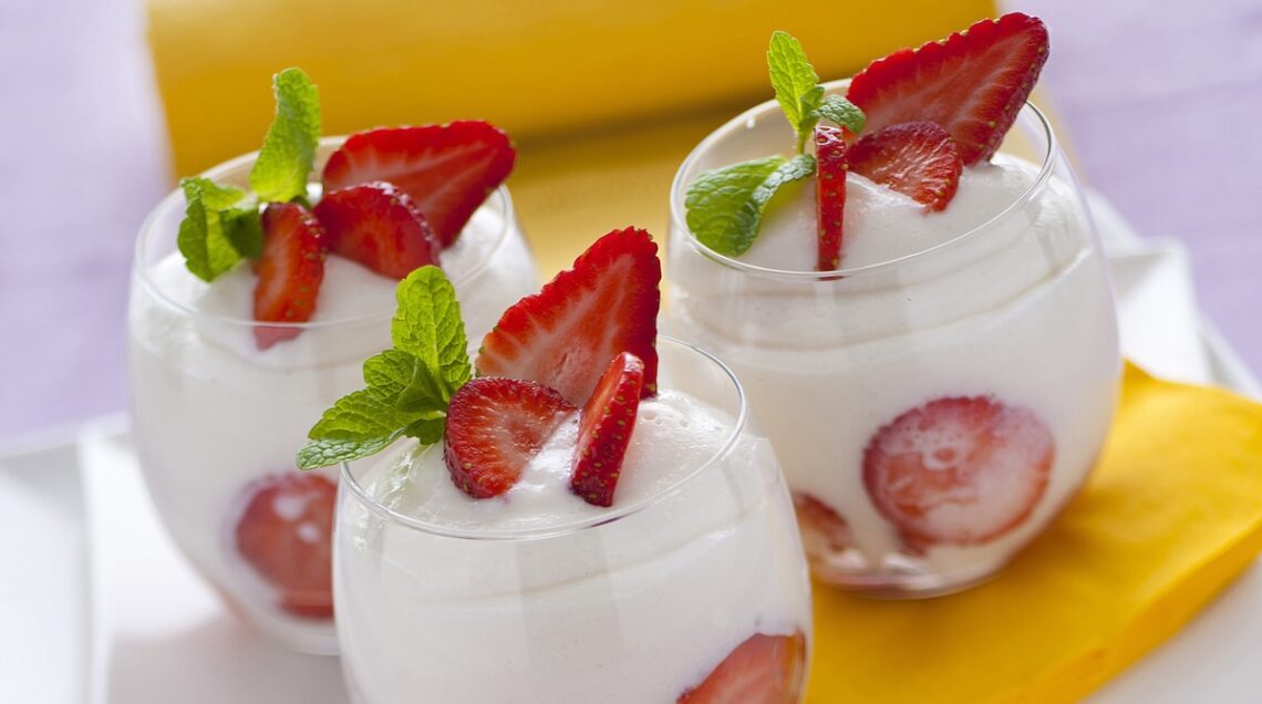 Mousse con fragole e limoncello in tre bicchieri tondi ovali, sopra un tovagliolo giallo ocra