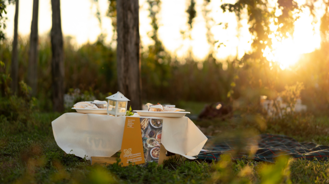 Tavolino da picnic allestito all'aperto al tramonto con piatti e depliant informativo "Io sono Friuli Venezia Giulia".
