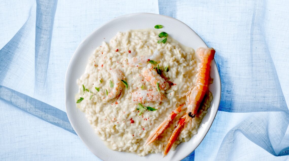 Risotto di mare alla maggiorana su sfondo azzurro servito all'interno di un piatto piano bianco