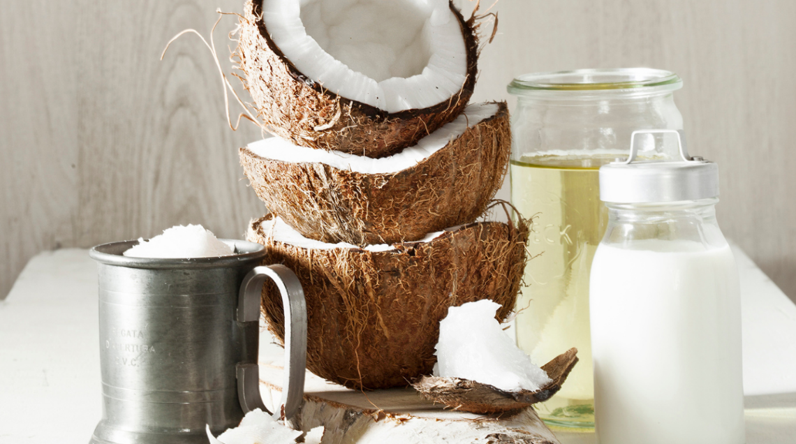 Partendo da sinistra: un bicchiere di metallo contenente polpa di cocco, tre gusci di cocco impilati, olio di cocco e latte di cocco
