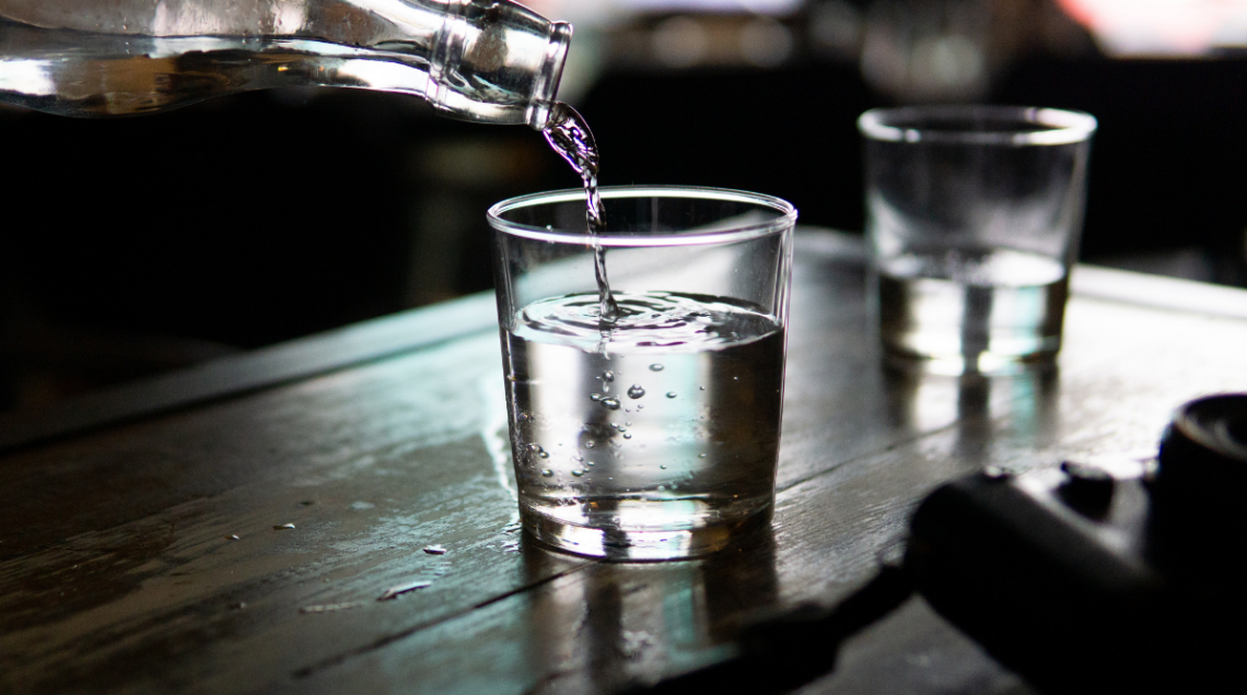 Un bicchiere di vetro trasparente mentre viene riempito di liquore all'anice da una bottiglia