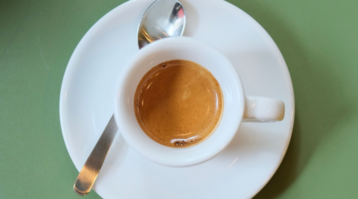 Caff&egrave; ristretto all'interno di una tazzina bianca appoggiata su un piattino con un cucchiaino di metallo