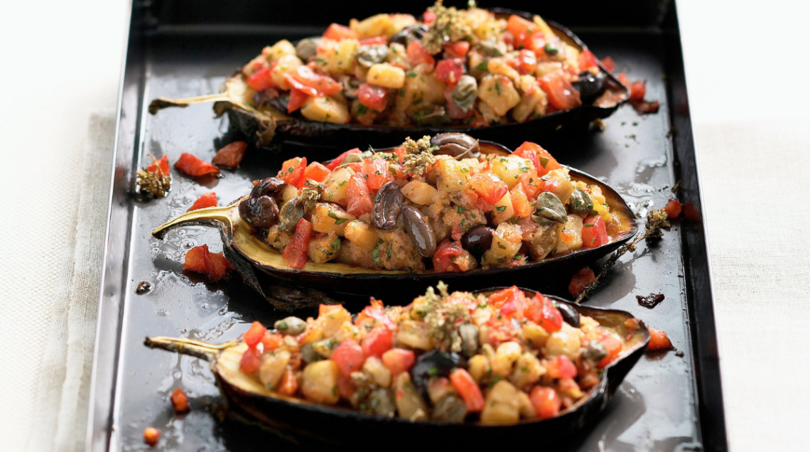 Tre melanzane al forno ripiene con capperi e olive su piatto rettangolare nero