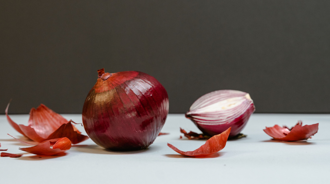 Qualche pezzo di buccia di cipolla rossa, una cipolla rossa intera e una cipolla rossa tagliata a metà su sfondo neutro