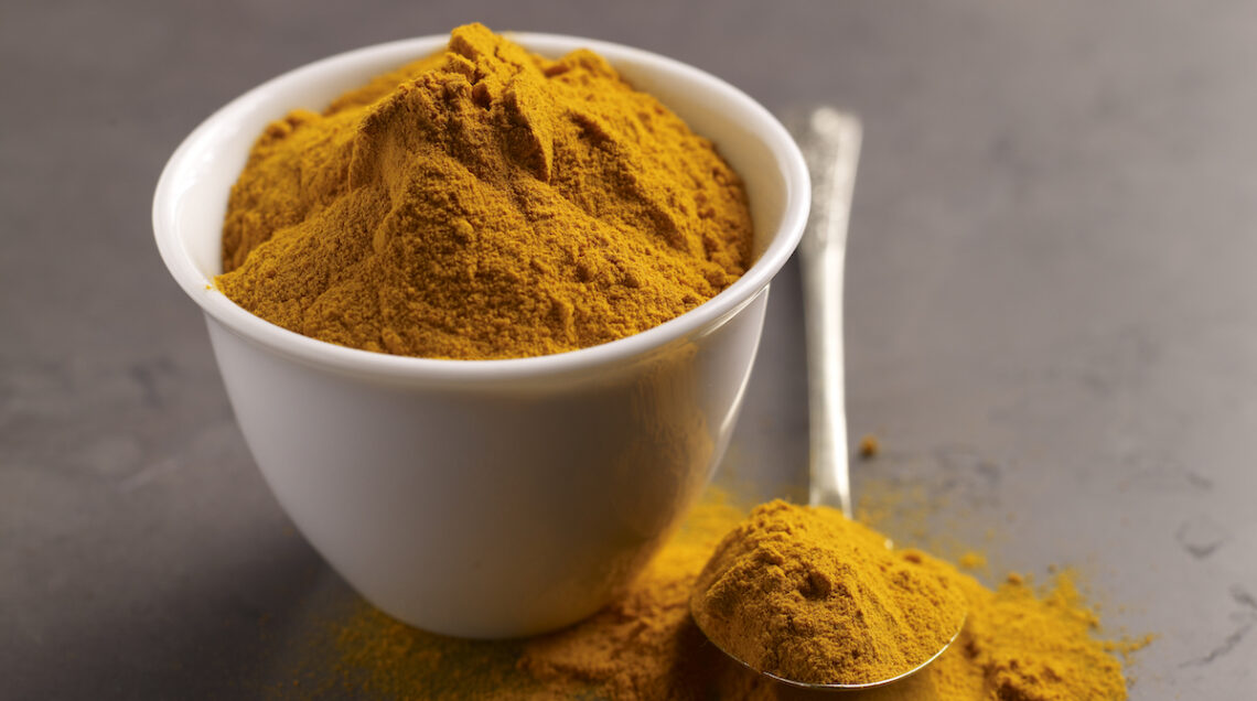 Curcuma in polvere all'interno di una ciotolina bianca con cucchiaio colmo di polvere