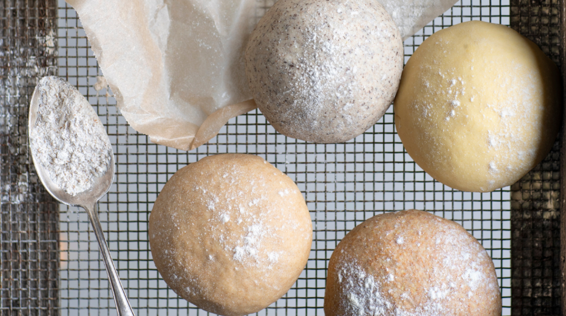 quattro palline di impasto, realizzate con farine differente, su una griglia con affianco un cucchiaio colmo di farina bianca
