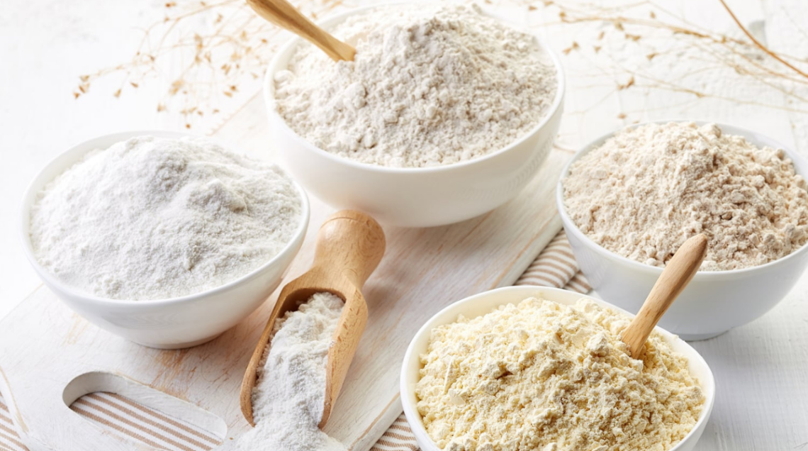 quattro ciotole bianche contengono quattro farine diverse e una paletta di legno contiene farina bianca