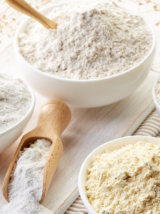quattro ciotole bianche contengono quattro farine diverse e una paletta di legno contiene farina bianca