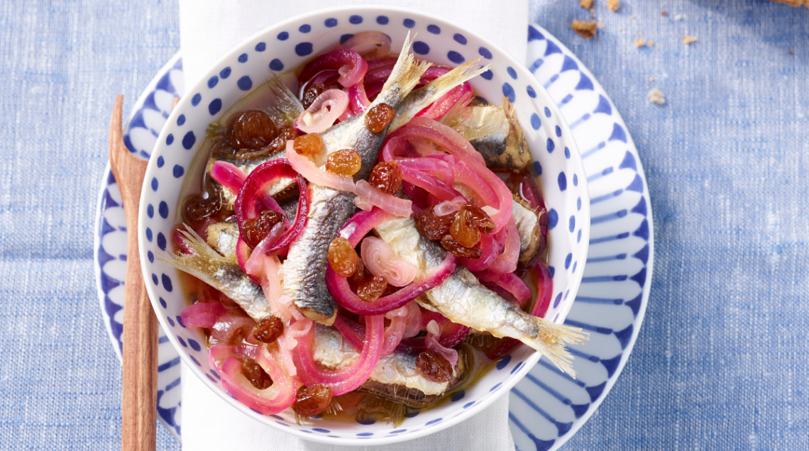 Tavola apprecchiata con un piatto piano e uno fondo con dettagli blu, contenente le sarde in saor