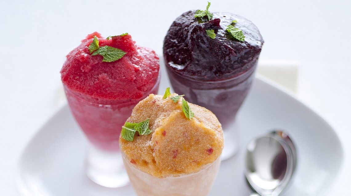 tre coppe con sorbetti di frutta diversa su un piatto con tre cucchiaini