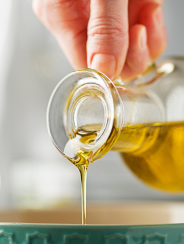 Una mano versa dell'olio in una ciotola verde