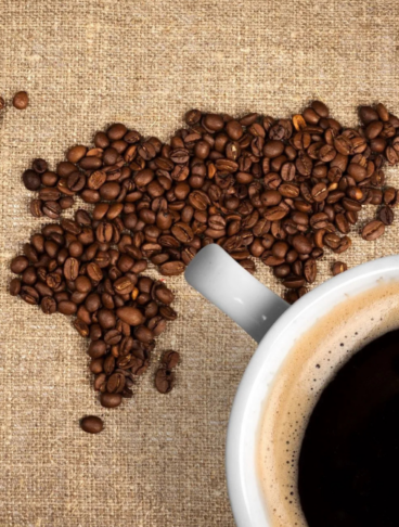 Una cartina, rappresentante diversi stati, fatta con chicchi di caffè. Affianco una tazza con del caffè