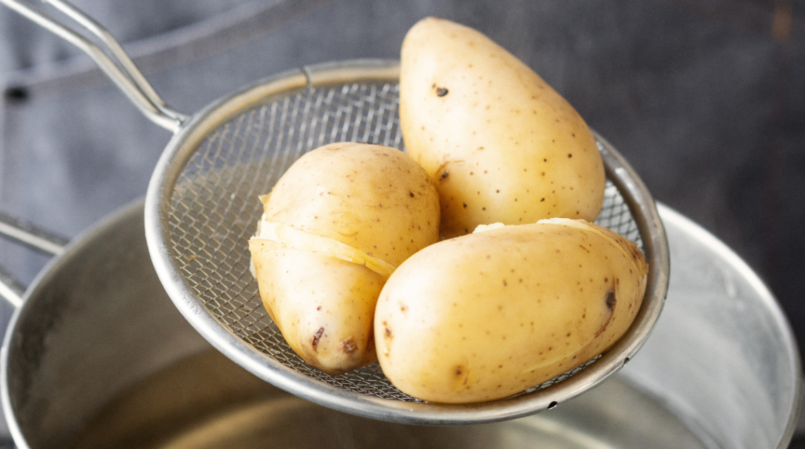 Un setaccio scola tre patate cotte in pentola