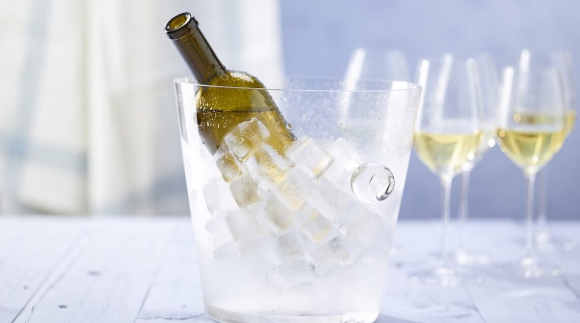 una bottiglia di vino nel secchiello del ghiaccio, dietro calici a cui &egrave; stato appena versato del bianco