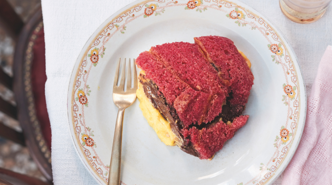 Una fetta di zuppa inglese su un piatto di ceramica con una forchetta d'oro, su una tovaglia bianca.