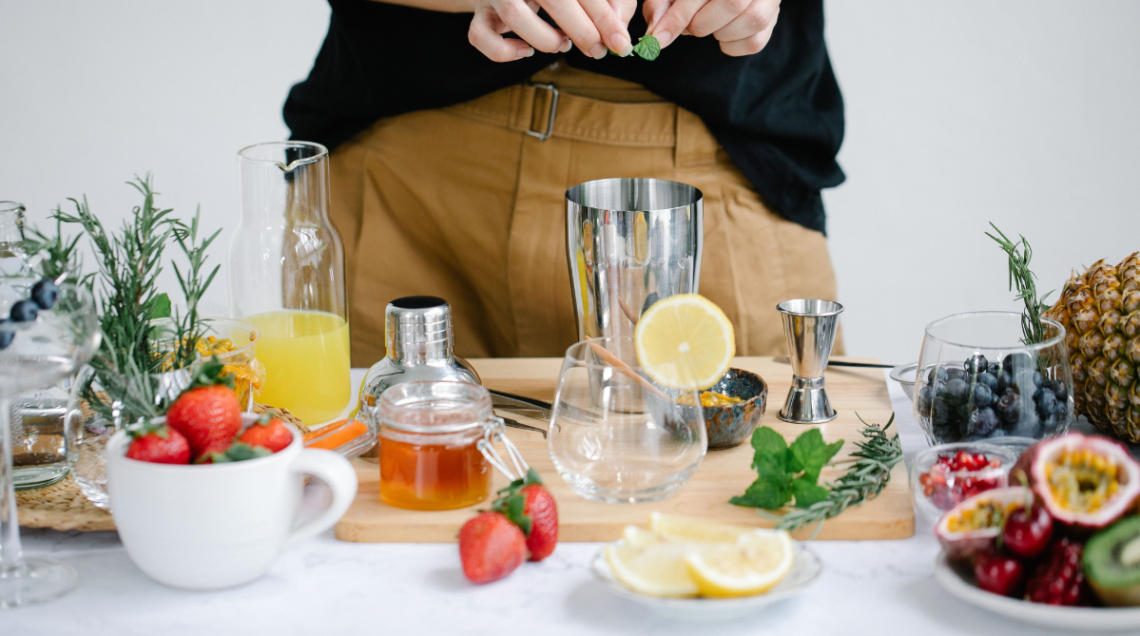 su un tavolo ci sono diversi strumenti, come lo shaker, e diversi ingredienti, come limone, frutta varie, erbe aromatiche ecc..., per la creazione di cocktail a basso contenuto alcolico