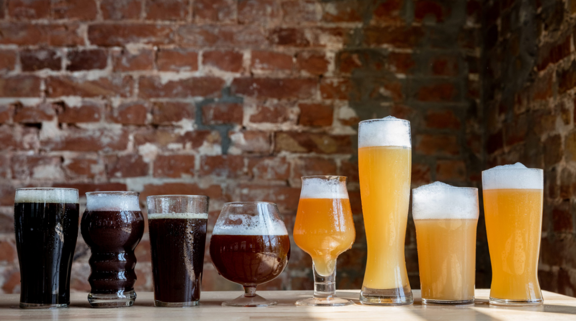 una serie di bicchieri di varie fogge, colmi di tipi di birra diversi, chiara, scura, densa e limpida