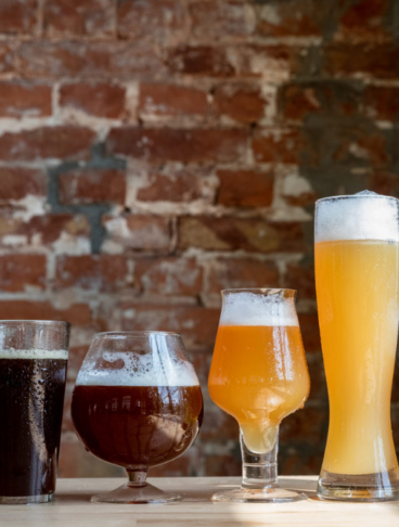 una serie di bicchieri di varie fogge, colmi di tipi di birra diversi, chiara, scura, densa e limpida
