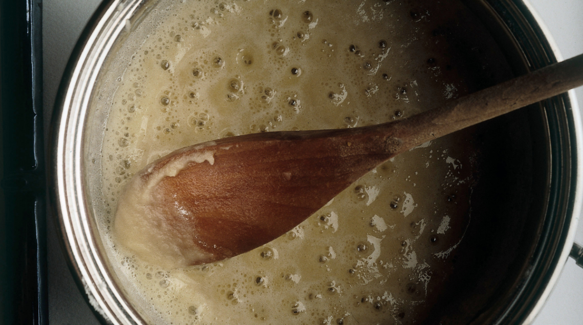 una pentola con del liquido sul fondo e un cucchiaio di legno