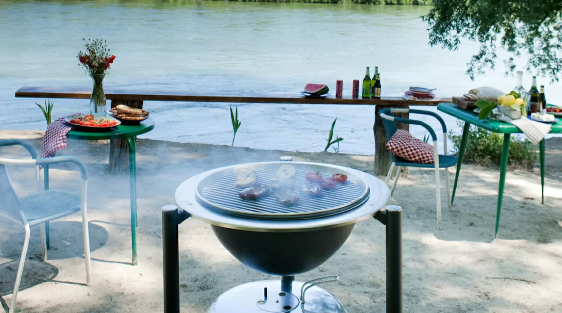 Di fronte a uno specchio d'acqua c'è una griglia rovente sopra la quale stanno cuocendo carne e verdure, delle sedie e dei tavolini. Tutto pronto per la grigliata estiva