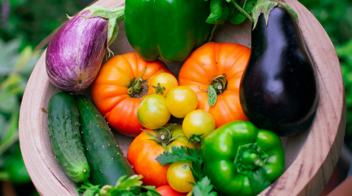 pomodori rossi, pomodori gialli, cetrioli, peperoni, melanzane, basilico in una ciotola di legno