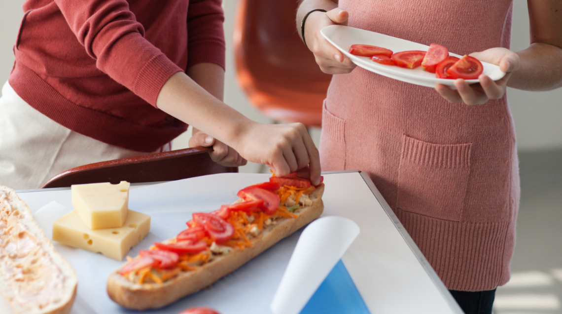 Due bambini stanno completando la farcitura di un panino con delle fette di pomodoro