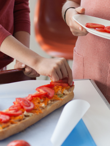 Due bambini stanno completando la farcitura di un panino con delle fette di pomodoro